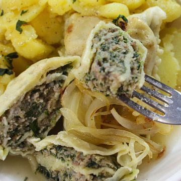 Maultaschen with caramelized onions and potato salad on a white plate.