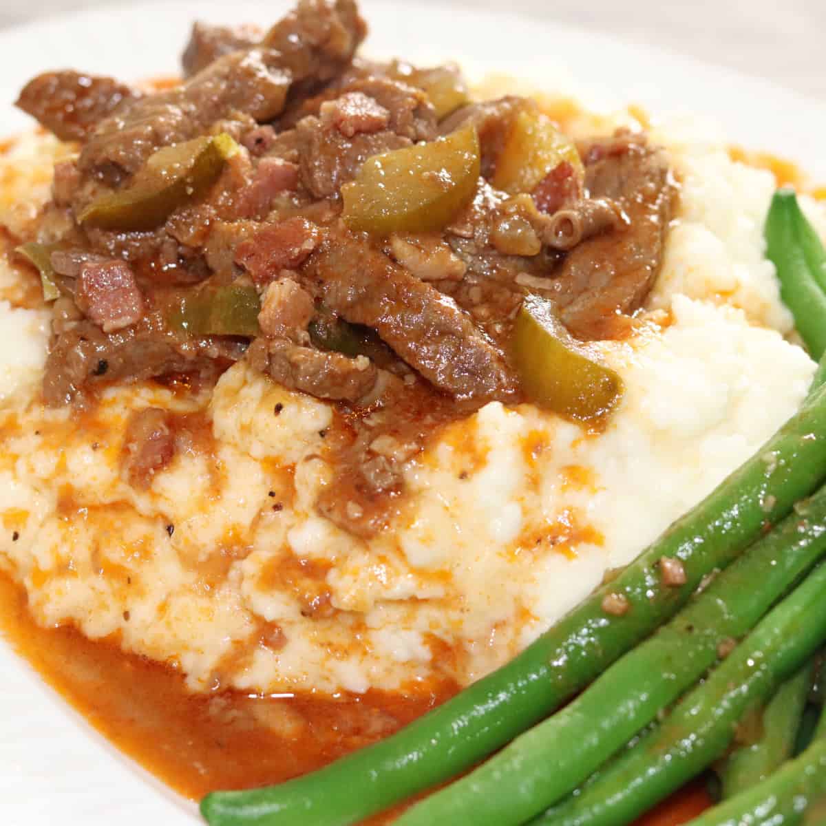 Rouladen stew on a bed of mashed potatoes and green beens on the side.
