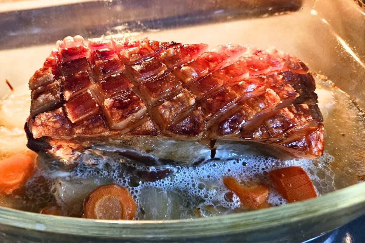 German pork roast with crispy crackling in a glass casserole dish cooking in the oven.