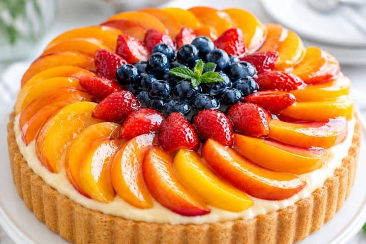 Colorful German Obsttorte fruit tart with strawberries, blueberries, and peaches for dessert.